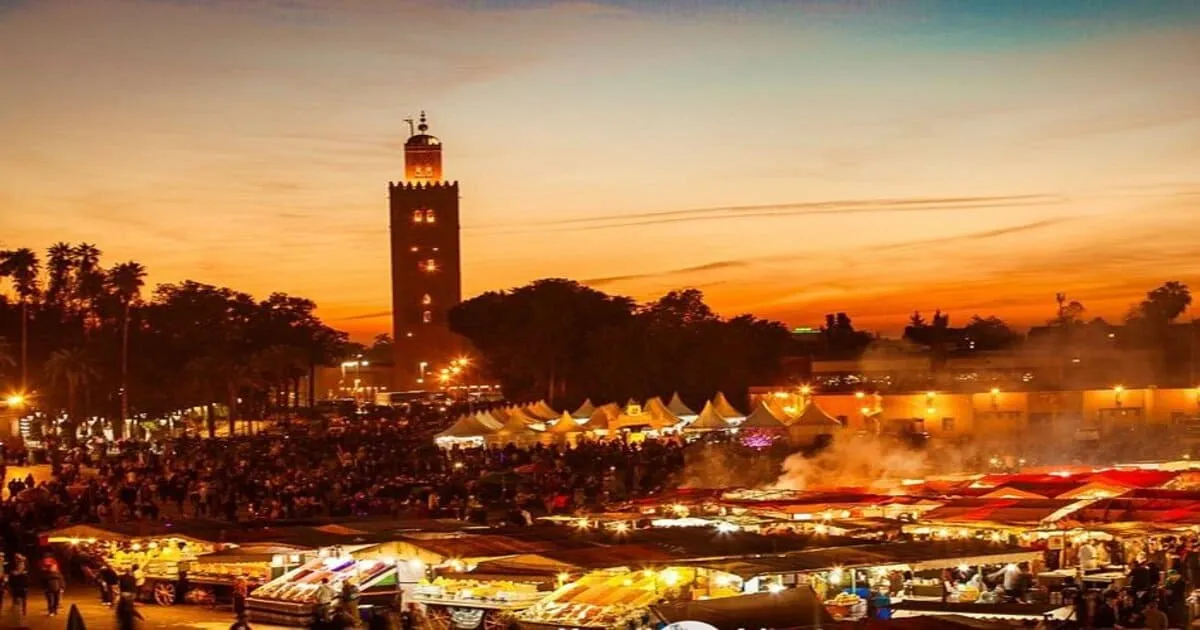Aerial view of Djemaa el Fna square in Marrakech at dusk, illuminated food stalls, crowd of visitors, Koutoubia minaret in background 