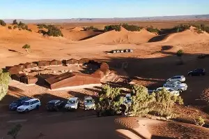 Secure parking area in Merzouga village with cars parked near desert dunes at sunset